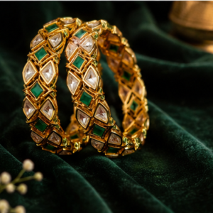 Pair of gold-plated broad bangles featuring a geometric lattice pattern of triangular bezel-set uncut Kundan polki stones and square emerald green center stones on green velvet by Glorious Jewels.