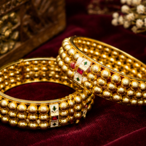 Pair of antique gold-plated broad bangles featuring three parallel rows of textured gold beads interspersed with white meenakari enamel blocks and ruby red stone accents from Glorious Jewels.
