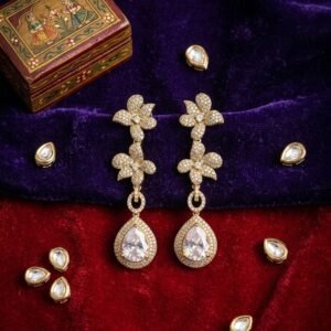 Handcrafted Antique gold dangle earrings featuring a double pavé-set floral cluster motif and a halo-framed pear-cut cubic zirconia teardrop stone displayed on velvet backdrop with Indian trinket box.