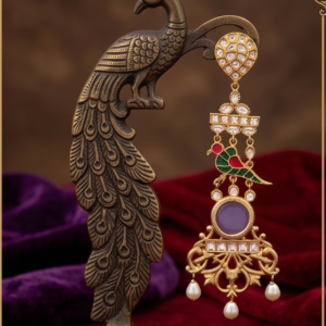 Antique gold long dangle earring featuring Kundan stonework, a red and green Meenakari bird motif, a round lavender cabochon centerpiece, intricate filigree, and dangling pearl drops displayed on a brass peacock stand over red velvet.